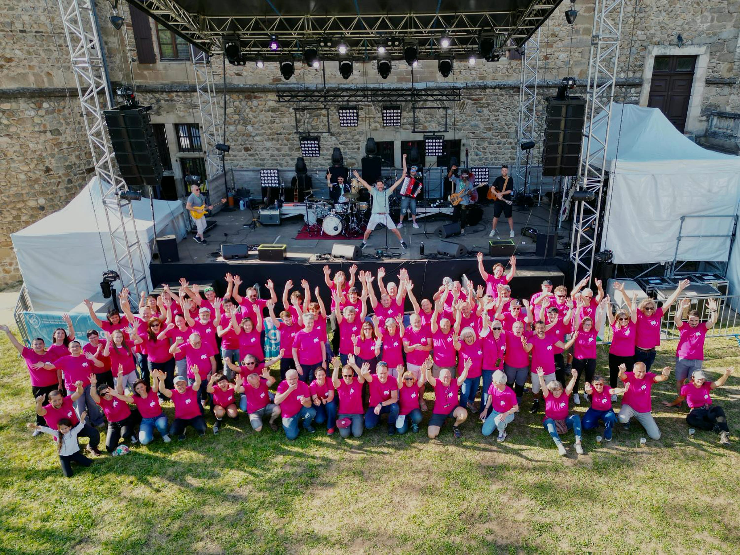 Vue aérienne des bénévoles du Festival des Pattes de Sanglier en t-shirts roses, bras levés devant la scène, édition 2026
