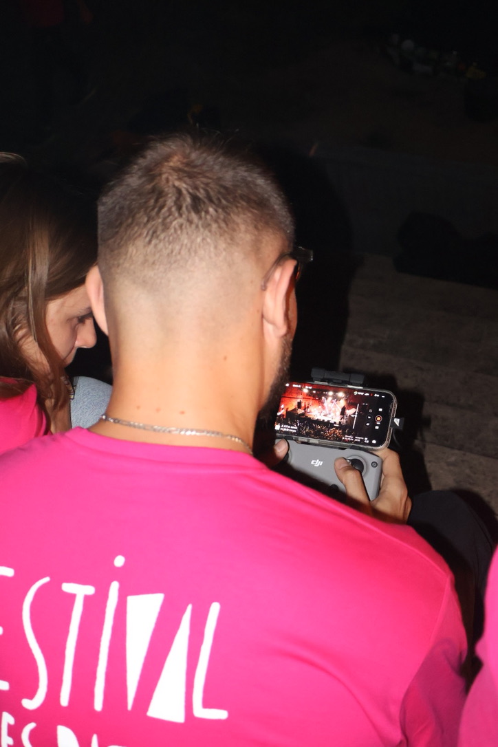 Clément Rancier, de dos en t-shirt du festival, pilote un drone et filme la scène du Festival des Pattes de Sanglier sur l'écran de sa télécommande